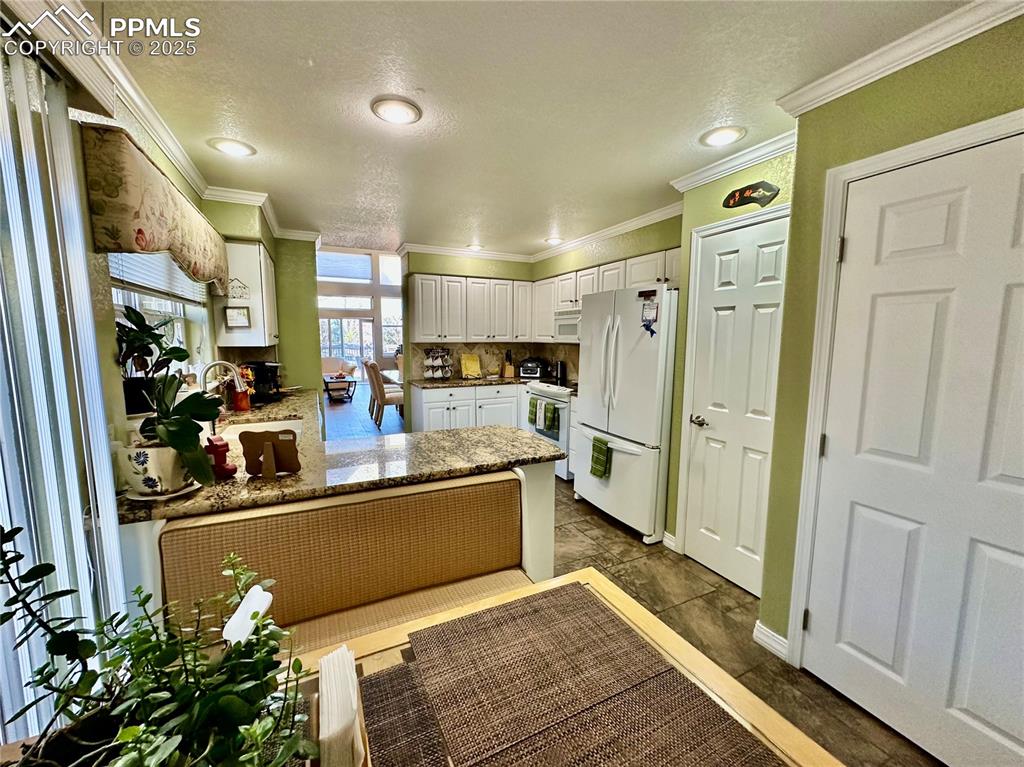Image 7 of 41: Kitchen with white appliances, white cabinets, dark stone countertops, orna