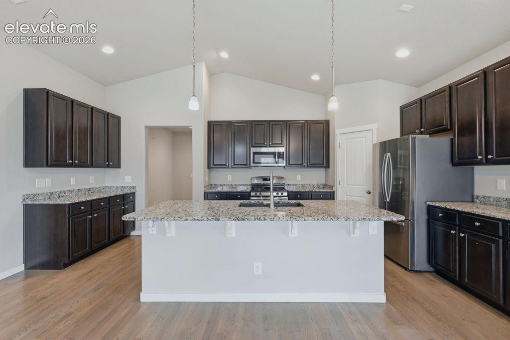 Image 12 of 40: Kitchen featuring a central island with a sink and pendant lighting, dark w