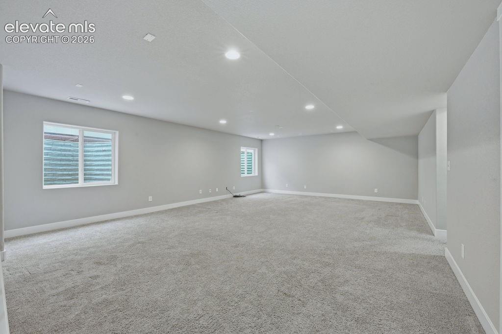 Image 29 of 40: Spacious room with recessed lighting, light gray walls, gray carpet, and tw
