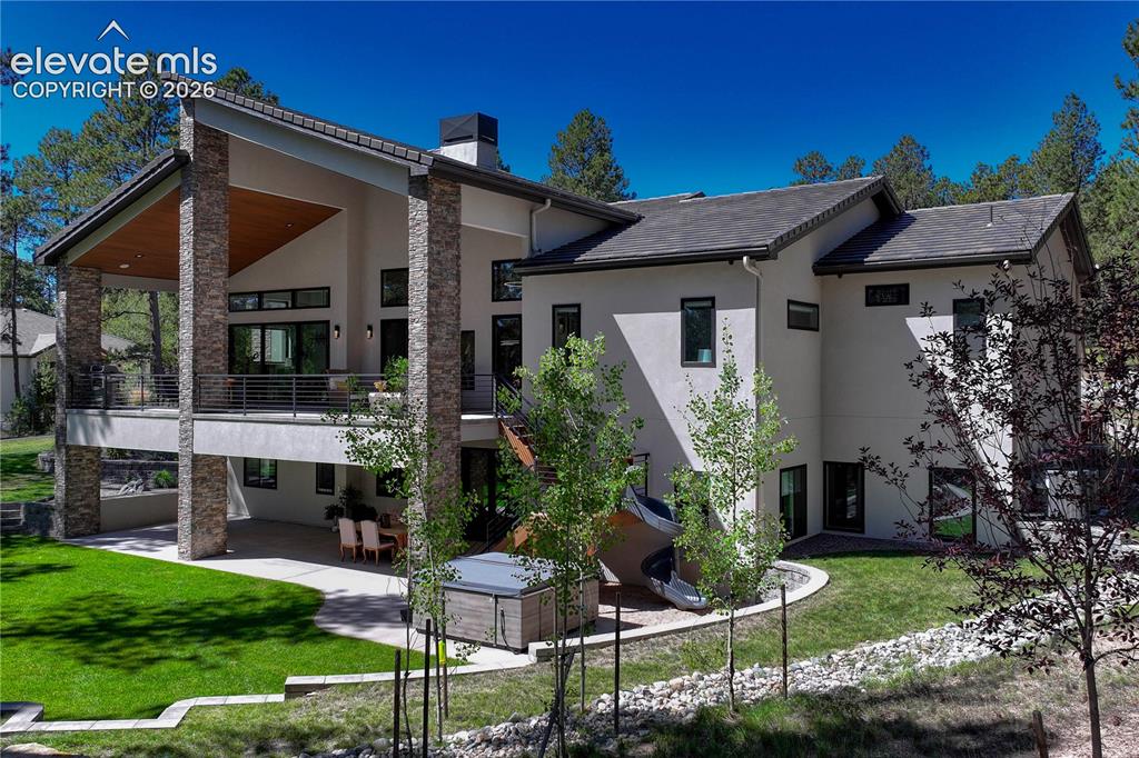 Image 3 of 49: Rear view of property featuring stucco siding, a patio area, a lawn, a chim