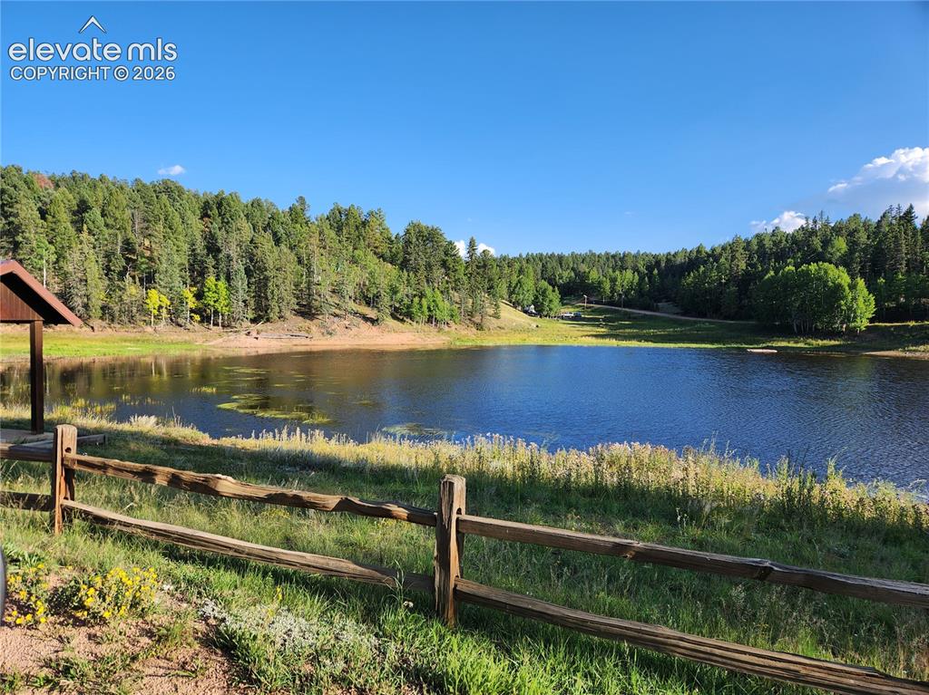 Image 19 of 39: Lakefront setting featuring a natural wood fence, mature trees, and a clear