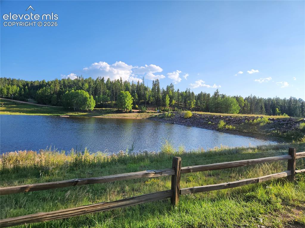 Image 20 of 39: Wood split-rail fence bordering a grassy area, a body of water, and a tree-