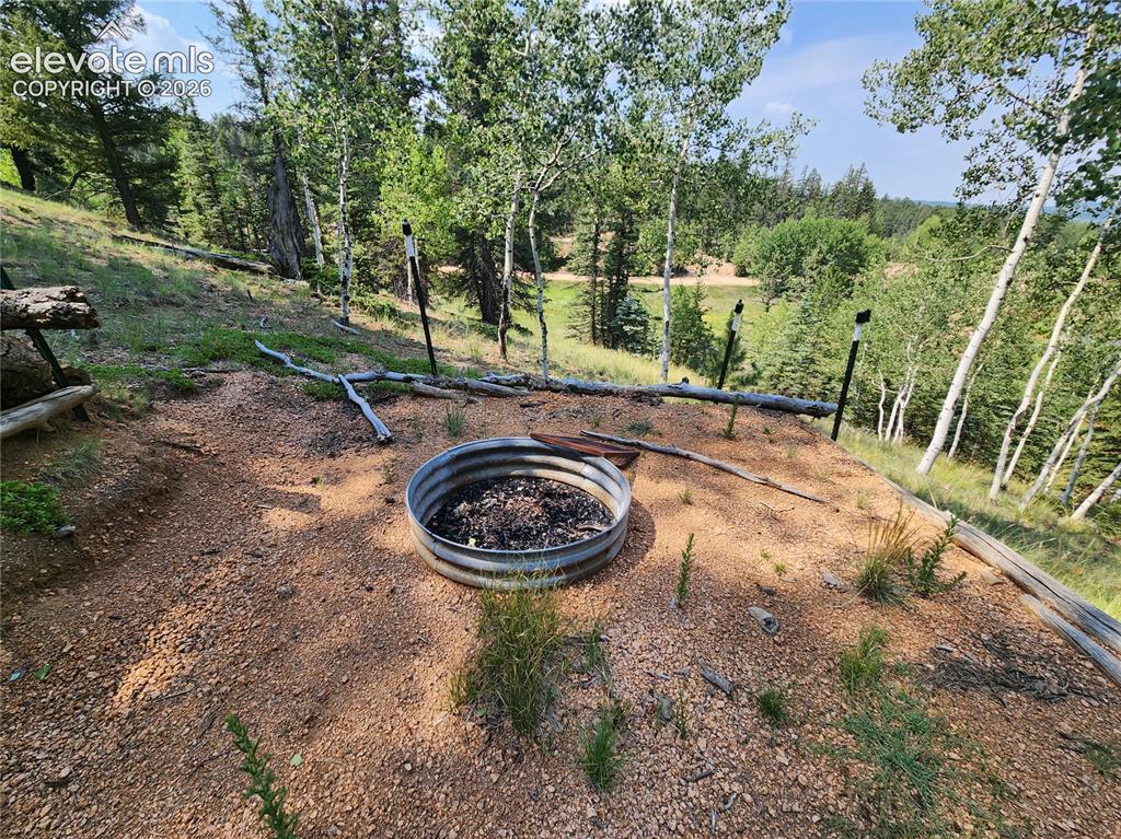 Image 37 of 39: Natural outdoor setting with a metal fire pit, surrounded by mature trees a