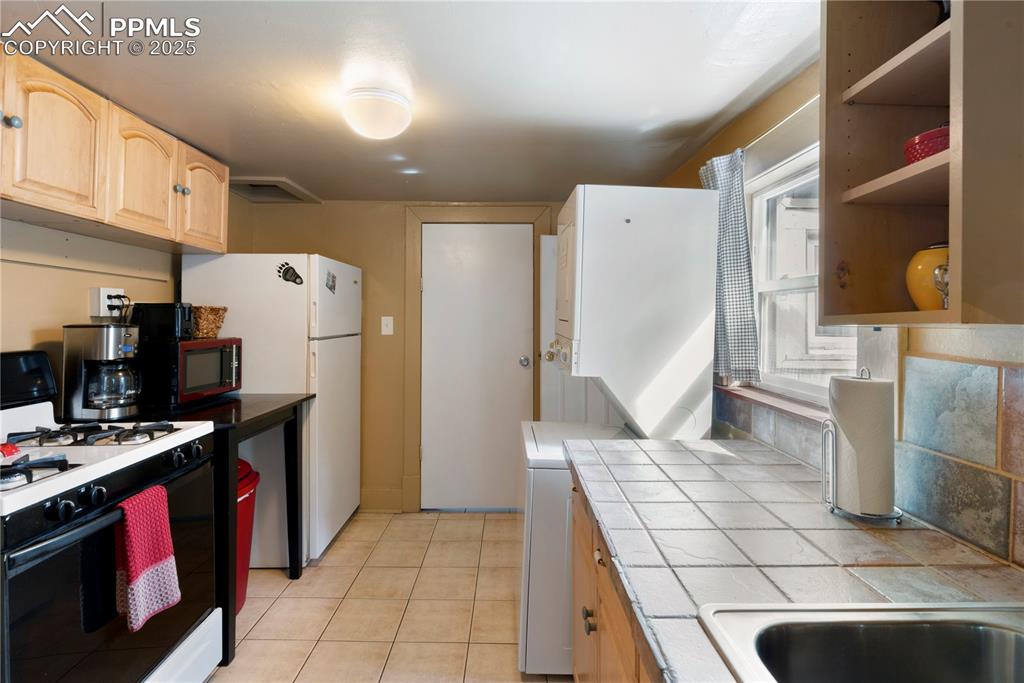 Image 6 of 15: Kitchen featuring white appliances, light brown cabinets, open shelves, lig