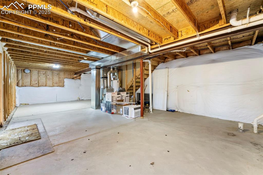 Image 21 of 31: Unfinished below grade area featuring stairway and water heater