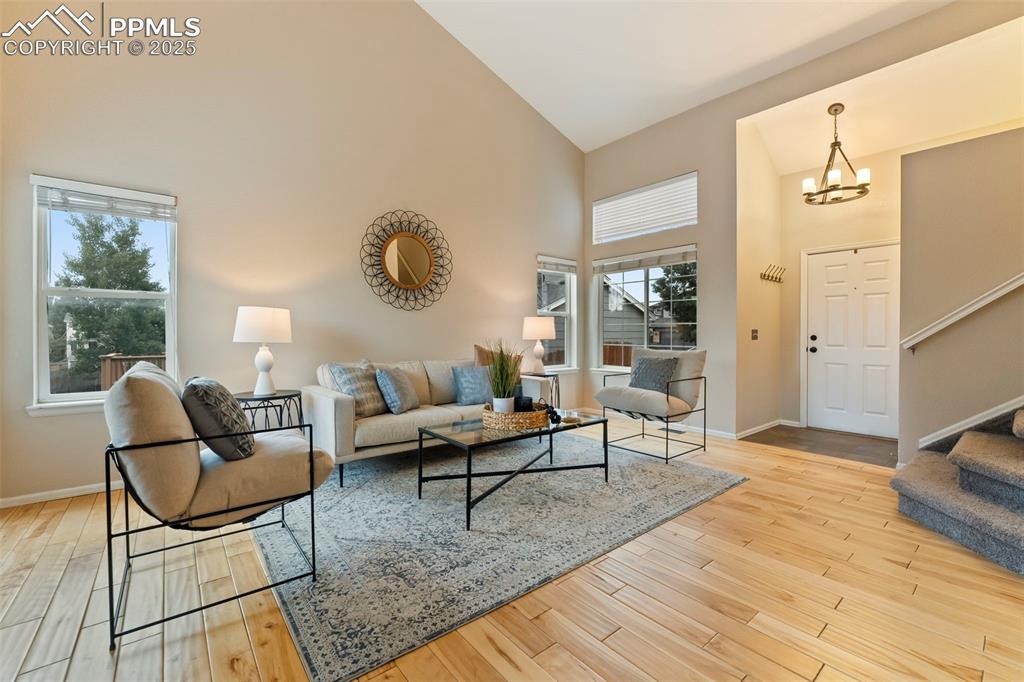 Image 4 of 31: Living area featuring high vaulted ceiling, a chandelier, stairs, and wood