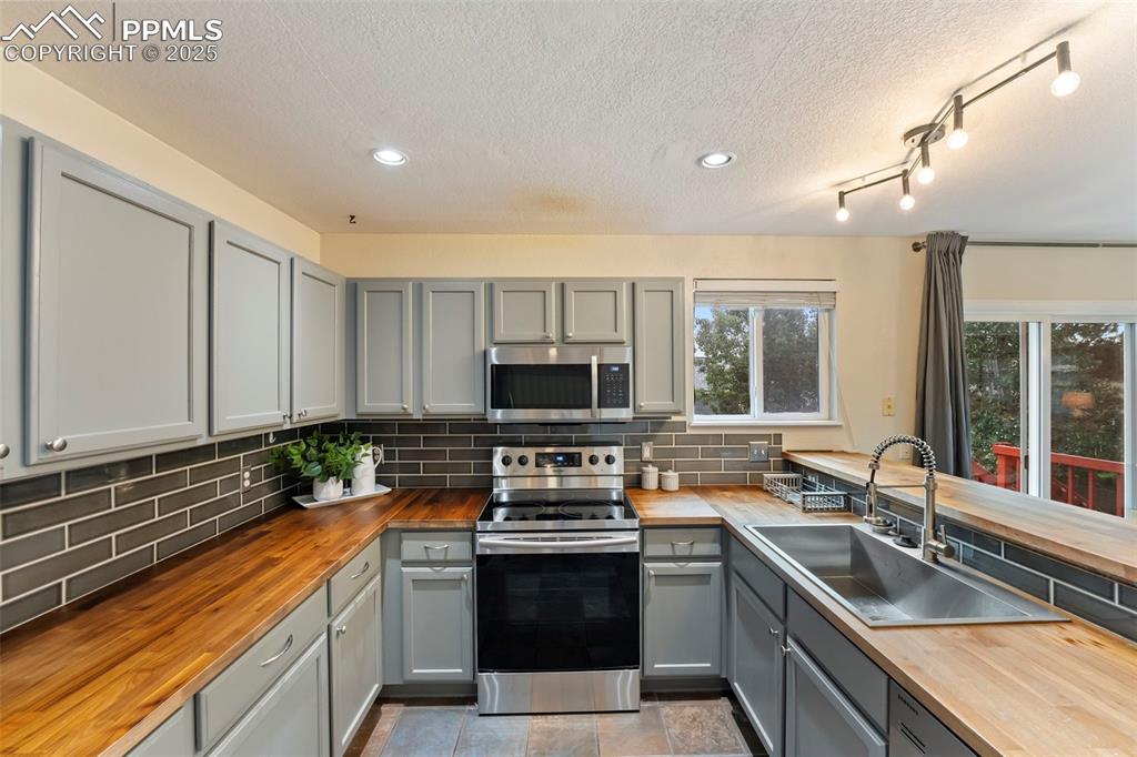 Image 7 of 31: Kitchen with wooden counters, gray cabinetry, appliances with stainless ste