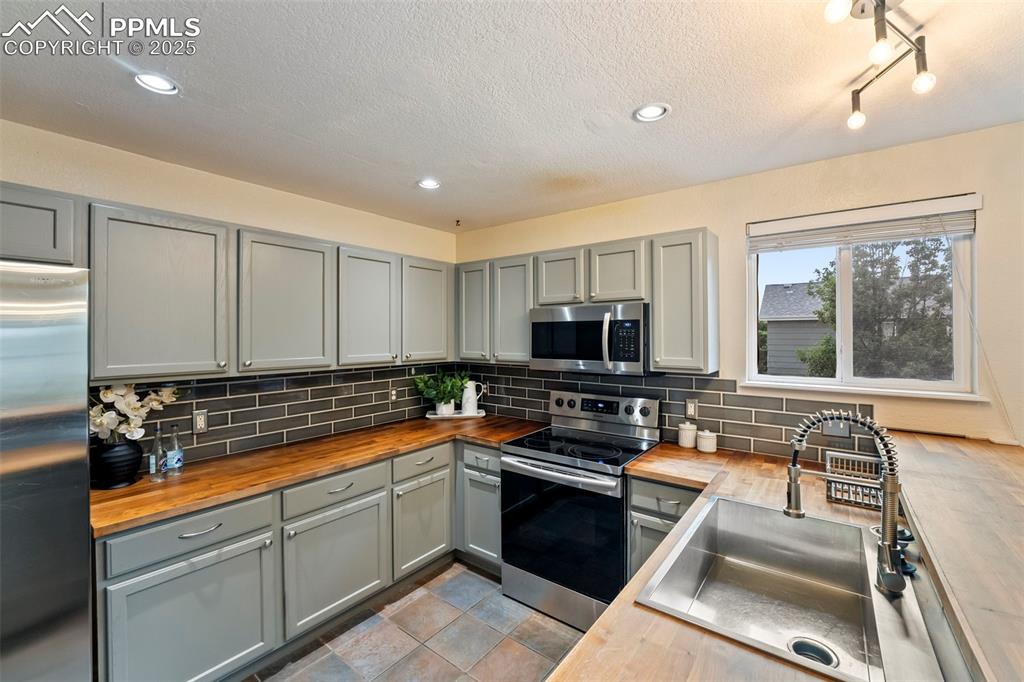 Image 8 of 31: Kitchen featuring butcher block counters, gray cabinetry, appliances with s