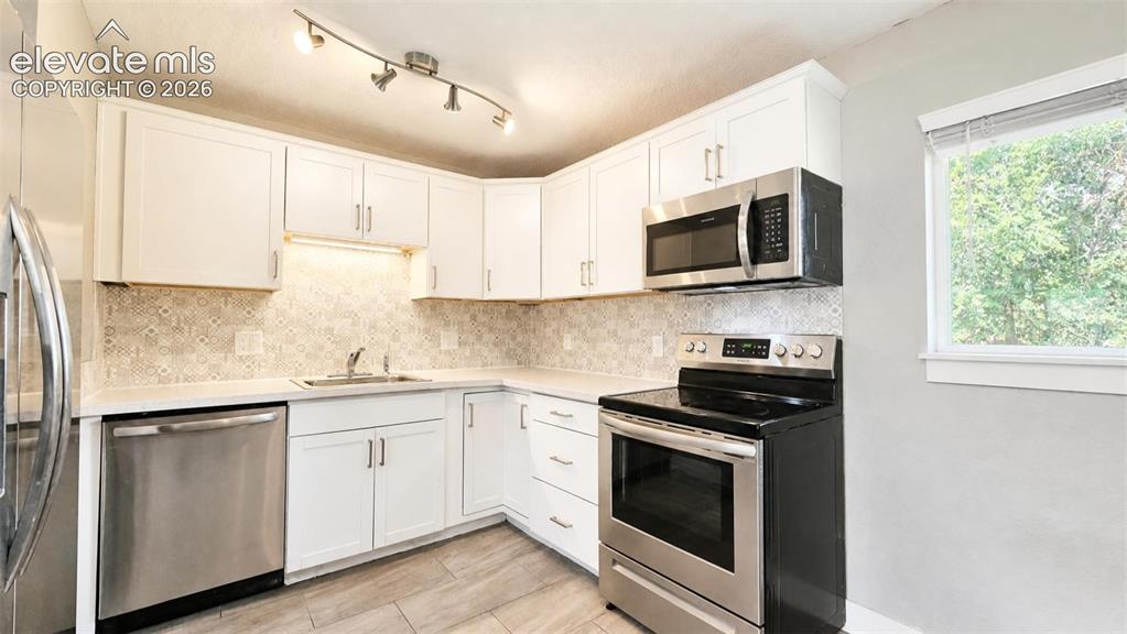 Image 7 of 31: Kitchen featuring white cabinetry, stainless steel appliances, a tile backs