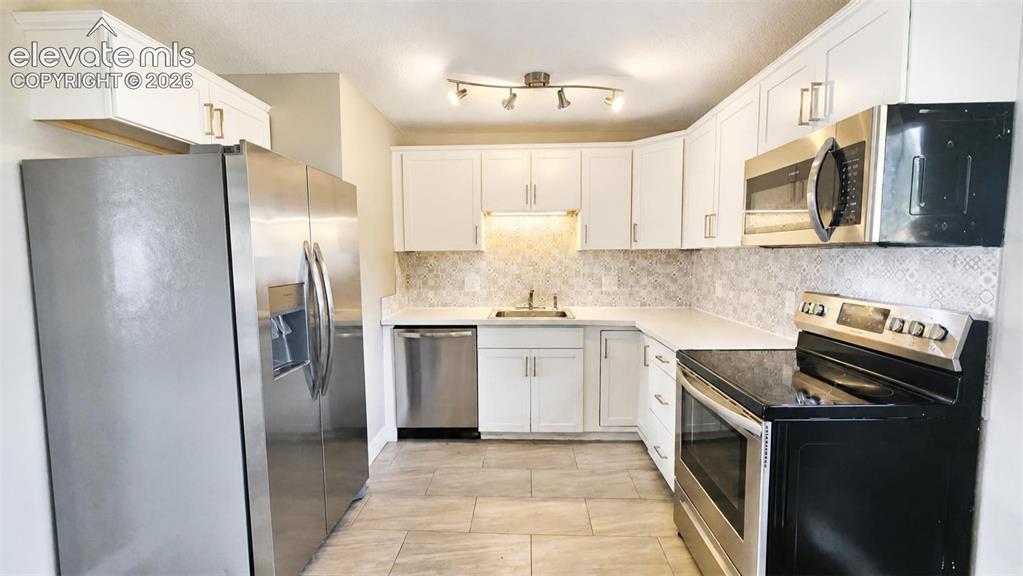 Image 8 of 31: Kitchen featuring white cabinetry, stainless steel appliances, a tile backs