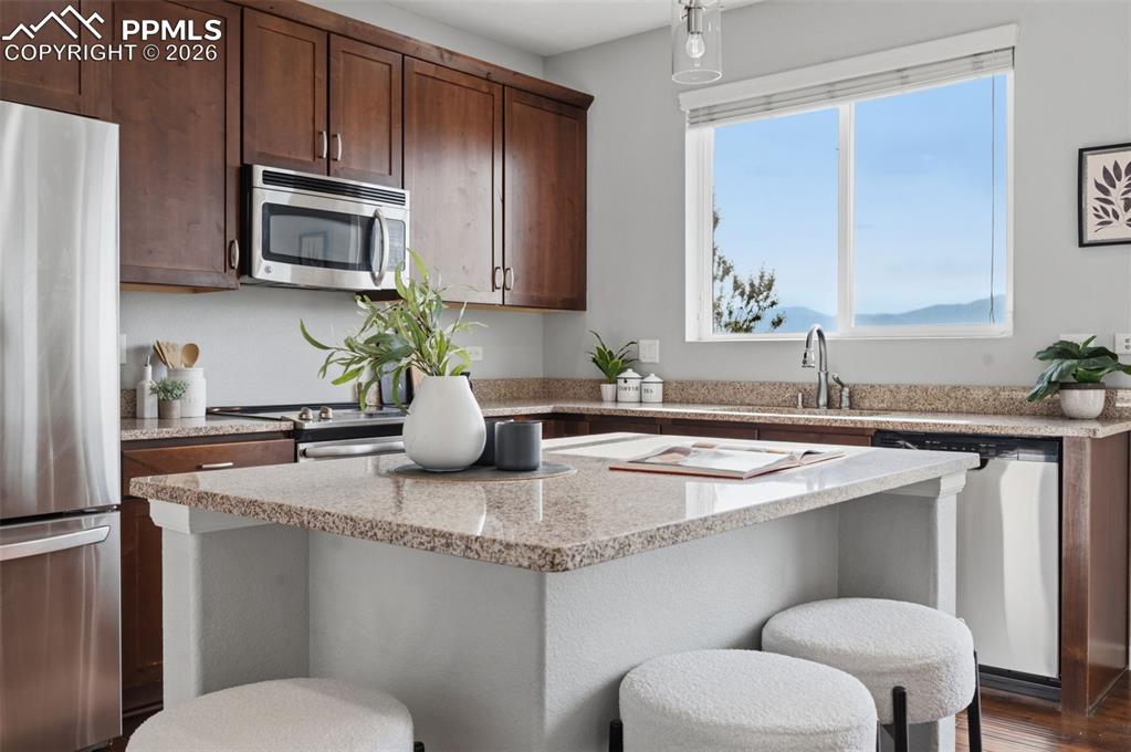 Image 12 of 49: Kitchen featuring a central island with a granite countertop, dark wood-fin