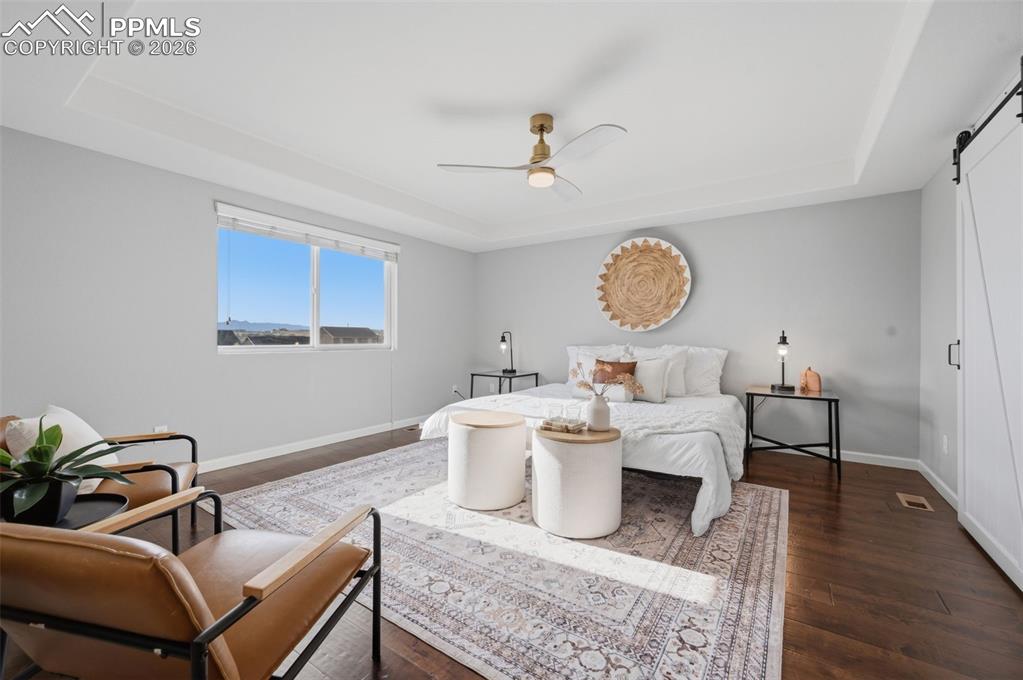 Image 18 of 49: Spacious bedroom featuring wood-finish flooring, a tray ceiling, and a mode