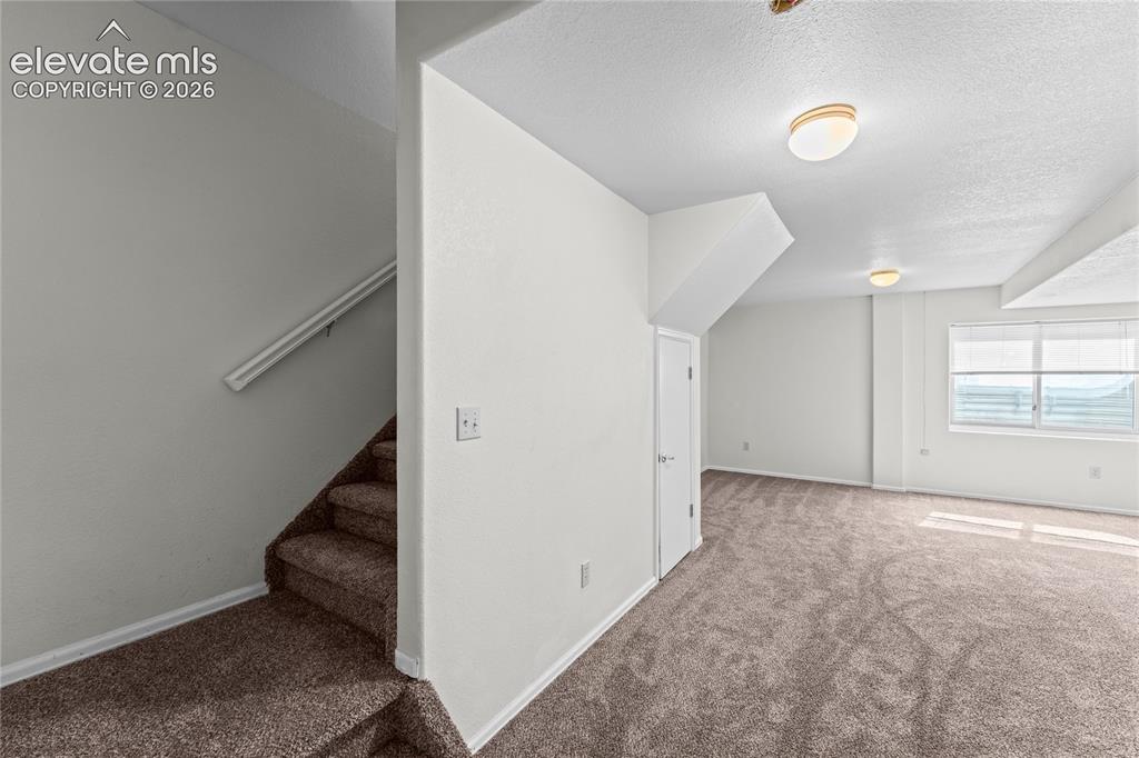 Image 23 of 43: Carpeted stairs with handrail leading to an open room featuring carpeted fl