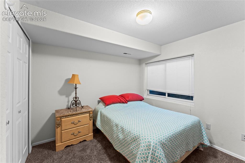 Image 27 of 43: White bi-fold closet doors, wall-to-wall carpeting, and a window with blind