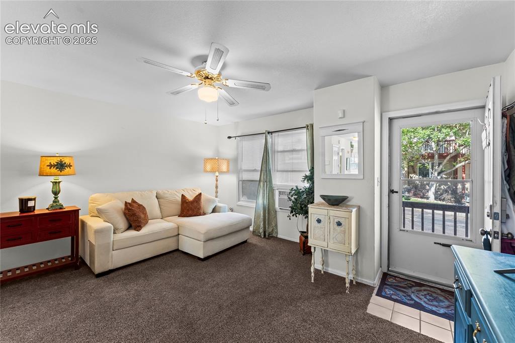 Image 3 of 43: Carpeted living area with a ceiling fan, white walls, and a window with bli
