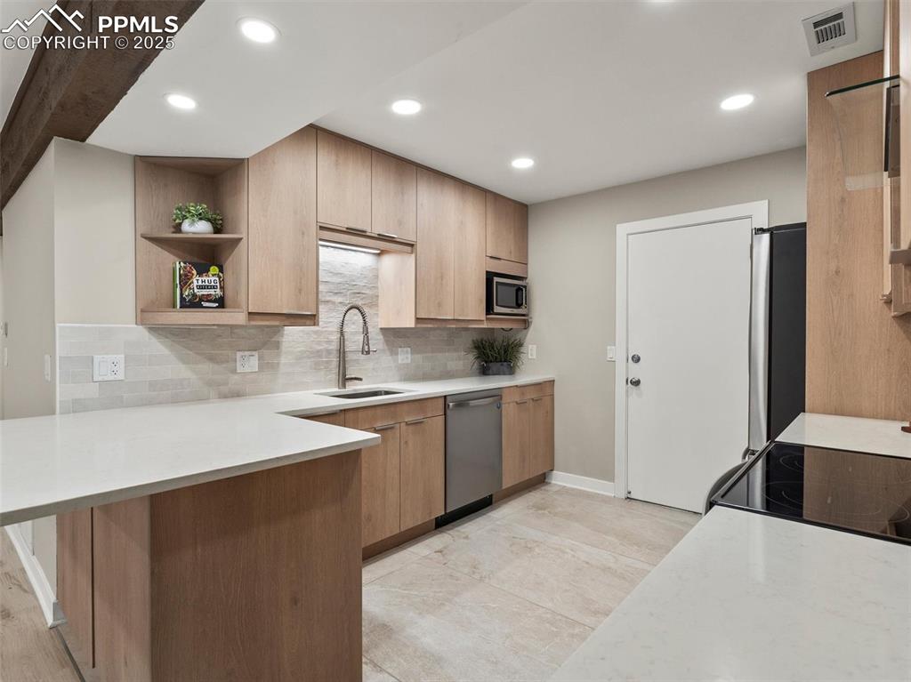 Image 14 of 36: Kitchen with a peninsula, light stone countertops, open shelves, tasteful b