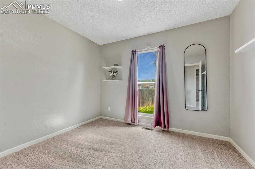 Image 20 of 42: Carpeted room with light gray walls, a window with a white frame, and built