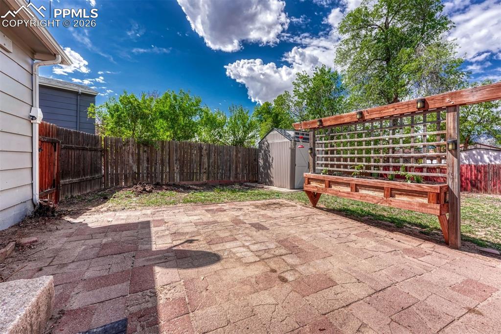 Image 34 of 42: Expansive brick paver patio featuring a built-in wooden trellis planter
