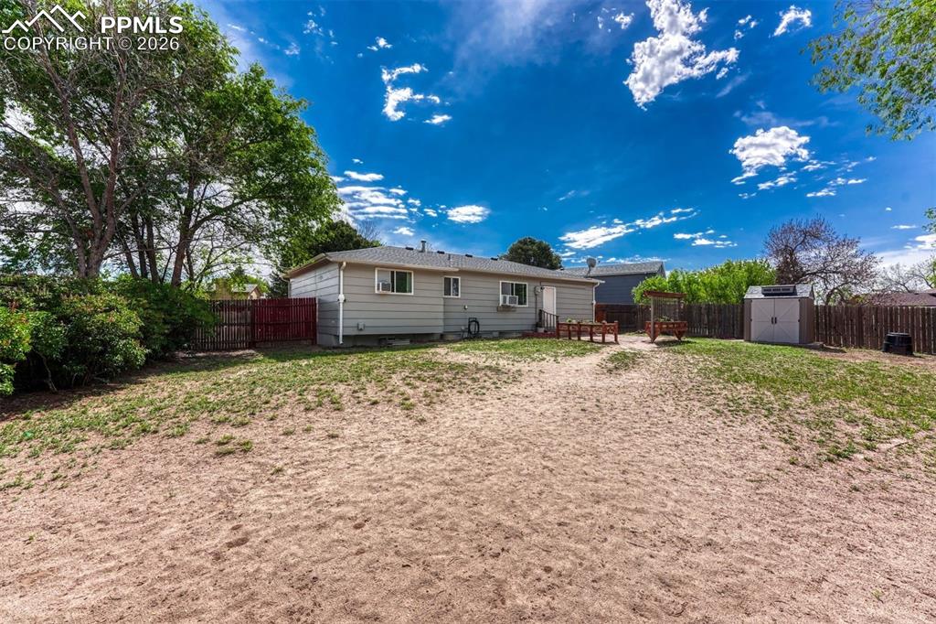 Image 39 of 42: Spacious backyard with partial fencing, mature trees, and a storage shed