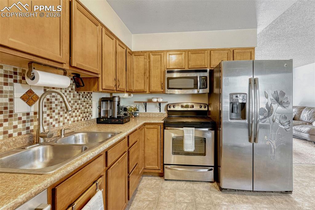 Image 7 of 42: Kitchen featuring light wood cabinetry, a mosaic tile backsplash, stainless