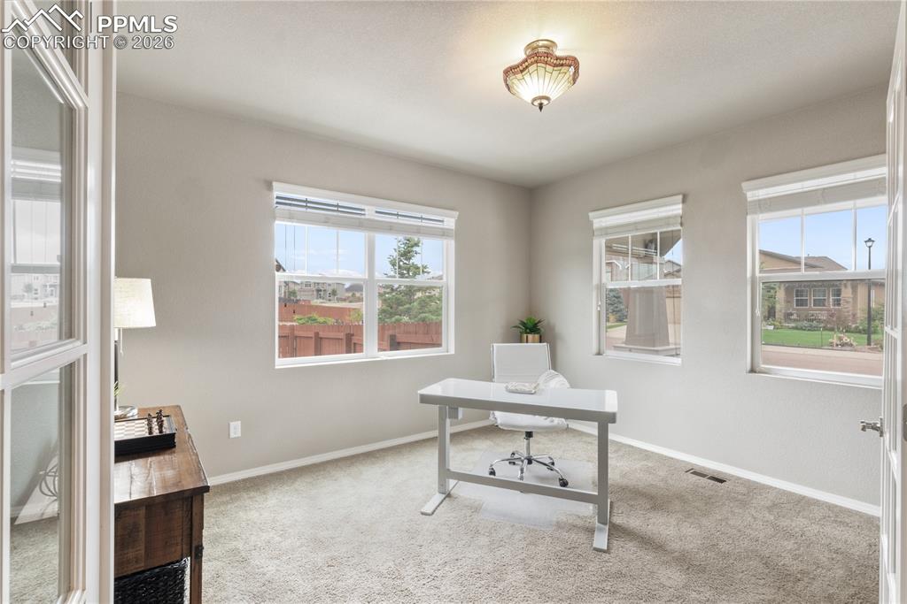 Image 12 of 50: Home office with light colored carpet and plenty of natural light