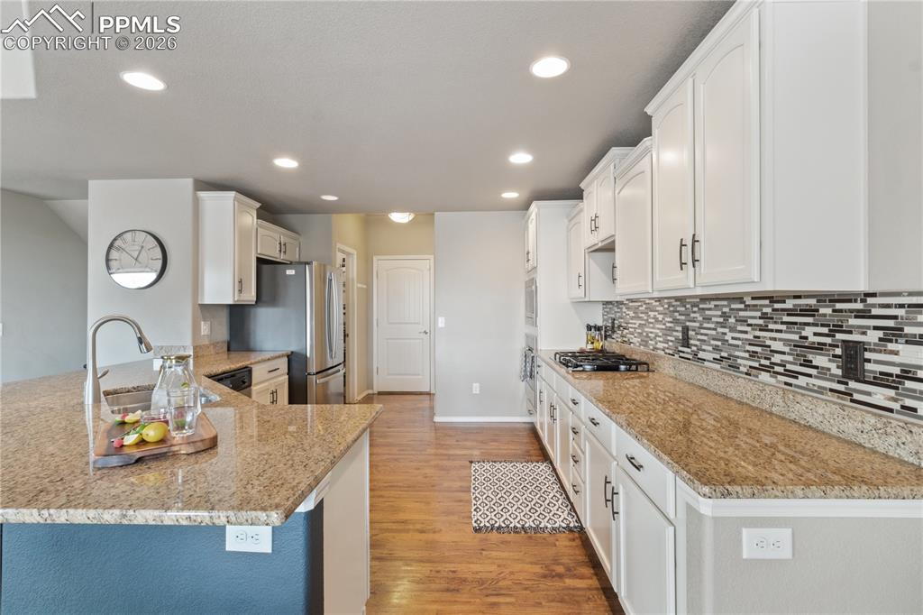 Image 18 of 50: Kitchen with light stone counters, a peninsula, light wood finished floors,