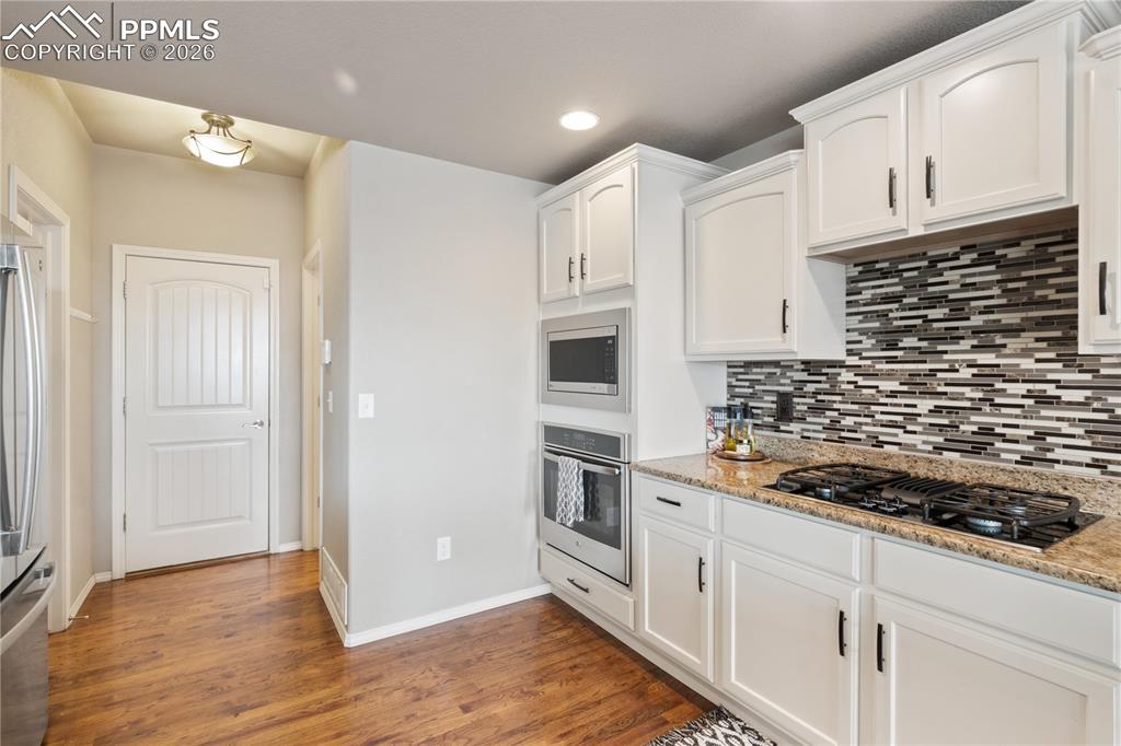 Image 20 of 50: Kitchen featuring stainless steel appliances, white cabinets, light stone c