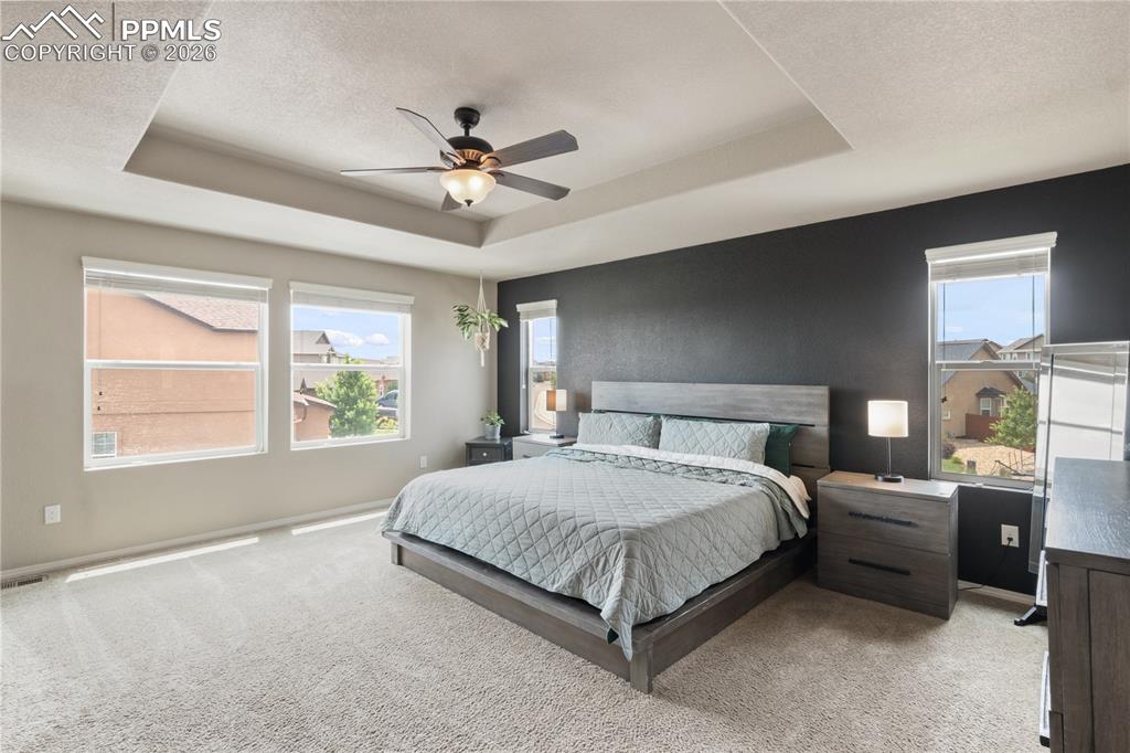 Image 24 of 50: Bedroom featuring light carpet, ceiling fan, a textured ceiling, and a tray