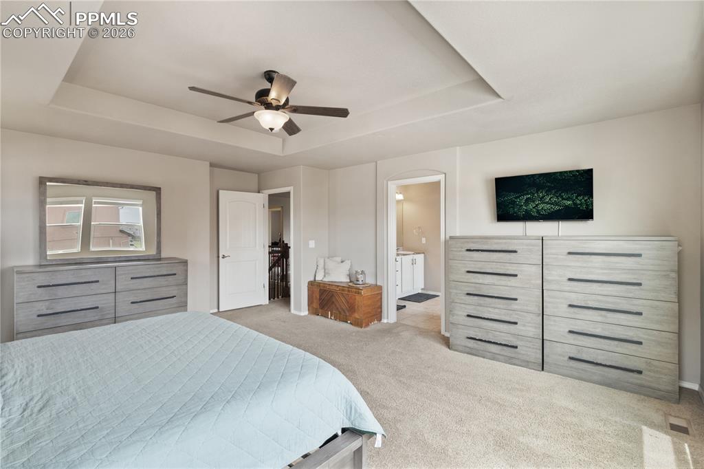 Image 26 of 50: Bedroom featuring light colored carpet, a raised ceiling, ceiling fan, and 