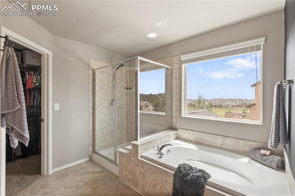 Image 27 of 50: Full bath with a walk in closet, a stall shower, a bath, and light tile pat