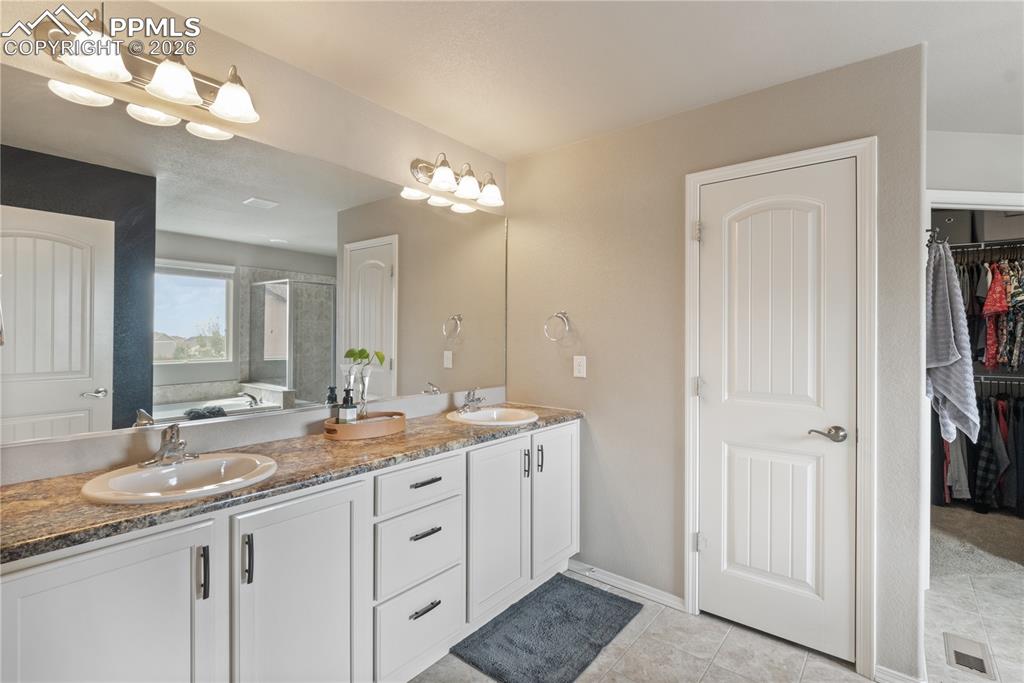 Image 28 of 50: Bathroom with double vanity, a shower stall, a walk in closet, a bath, and