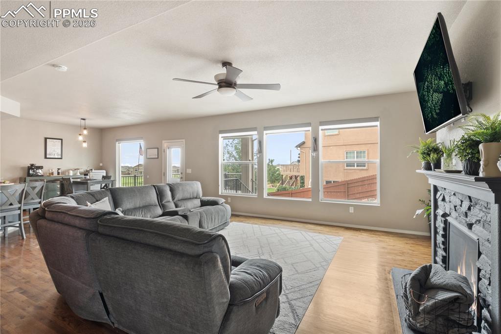 Image 9 of 50: Living room with wood finished floors, a stone fireplace, ceiling fan, and 
