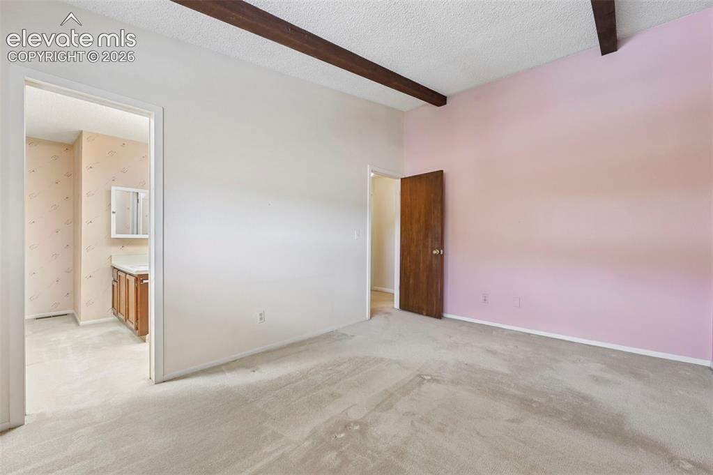 Image 17 of 24: Vaulted ceilings with exposed wood beams, carpeted flooring, and an en-suit