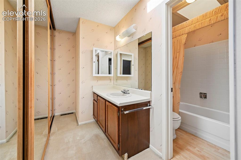 Image 18 of 24: Bathroom featuring a wood-finish vanity with countertop, wall-mounted mirro