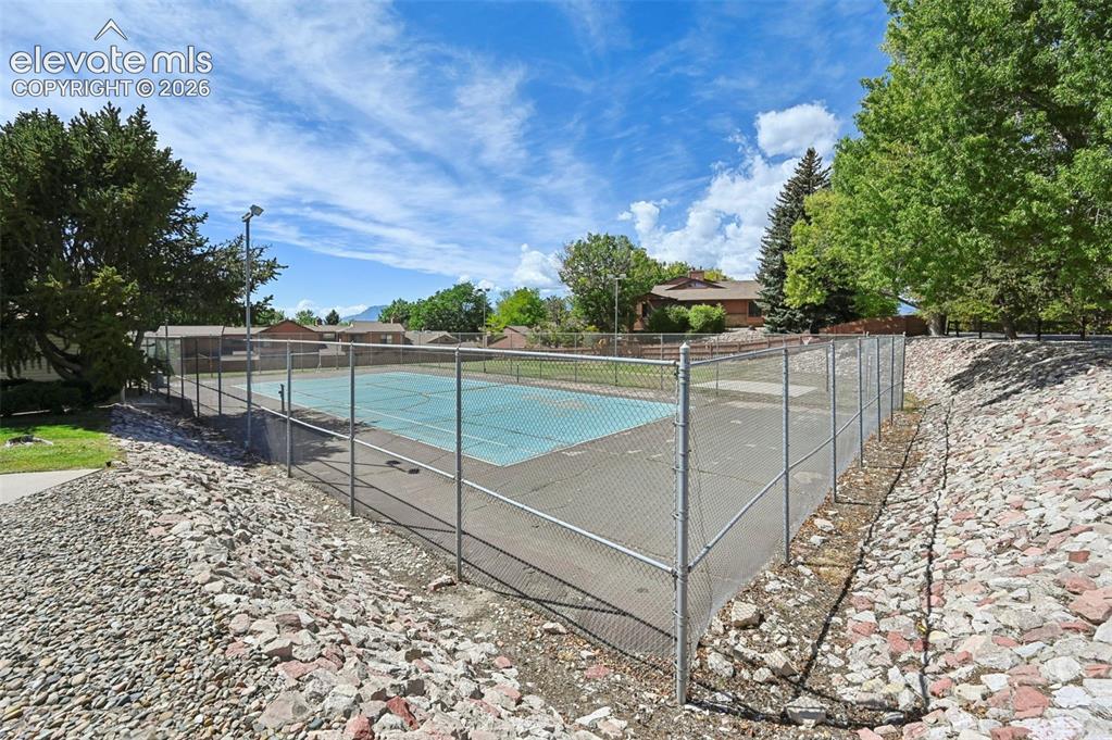 Image 23 of 24: Fenced outdoor court with a hard surface, featuring overhead lighting and s