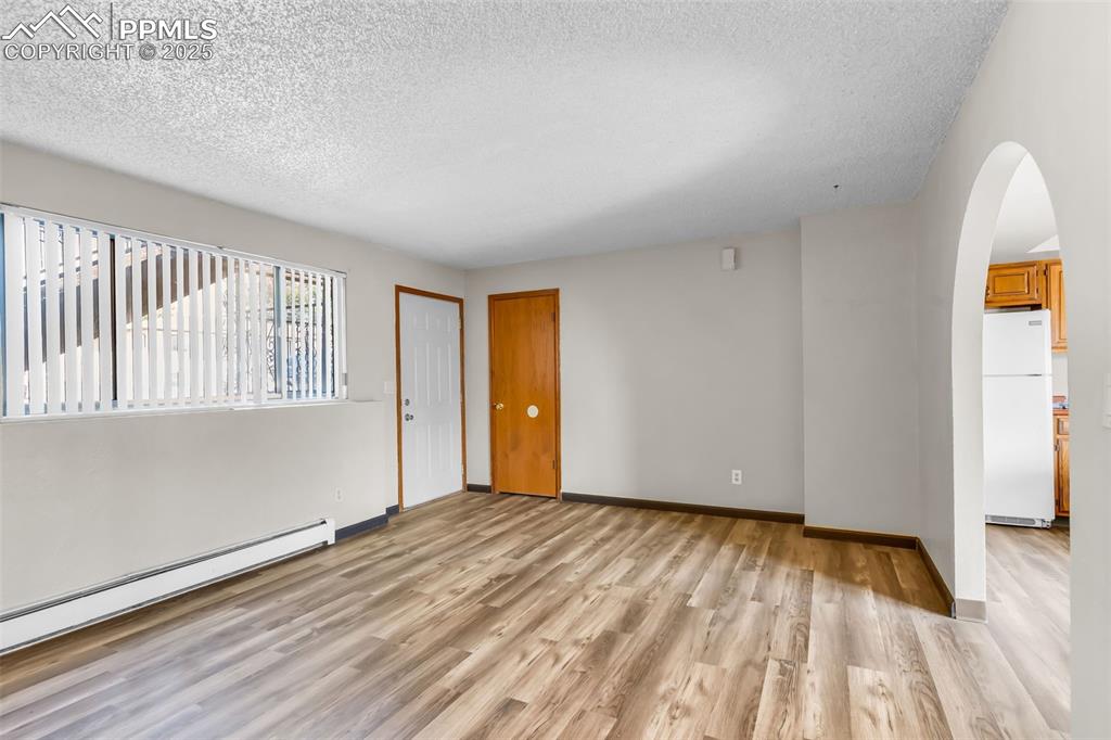 Image 15 of 26: Empty room with light wood finished floors, arched walkways, a textured cei