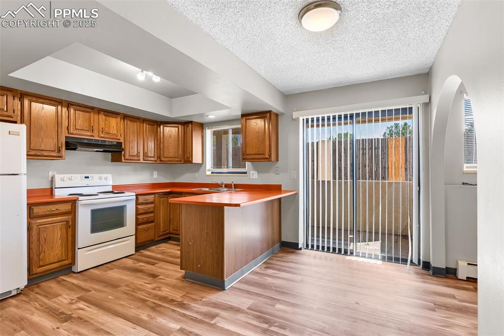 Image 16 of 26: Kitchen featuring brown cabinets, white appliances, light wood-type floorin