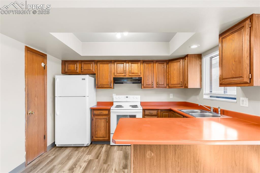 Image 17 of 26: Kitchen with white appliances, light wood-type flooring, a raised ceiling,