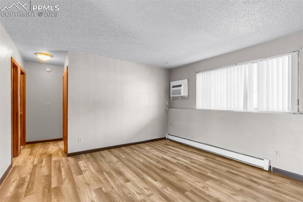 Image 21 of 26: Unfurnished room with a textured ceiling, baseboard heating, light wood fin