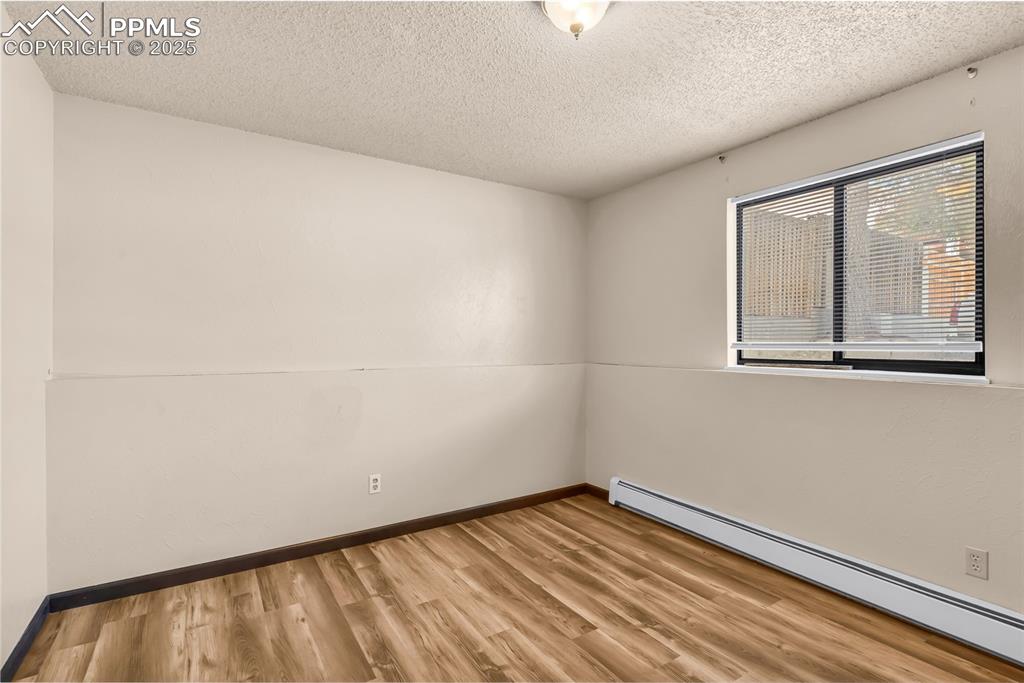 Image 23 of 26: Empty room featuring baseboard heating, light wood finished floors, and a t