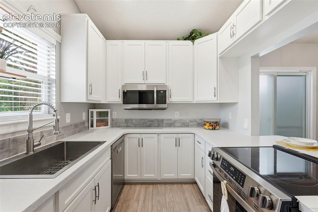 Image 12 of 45: U-shaped kitchen featuring white cabinetry, stainless steel appliances, lig