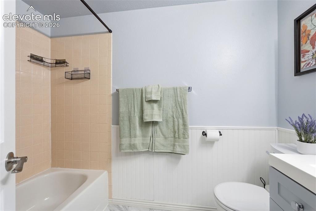 Image 27 of 45: Bathroom featuring a bathtub with tiled surround, white beadboard wainscoti