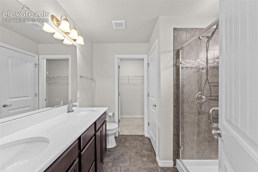 Image 14 of 40: Dual sink vanity with dark wood-finish cabinetry, a framed shower with tile