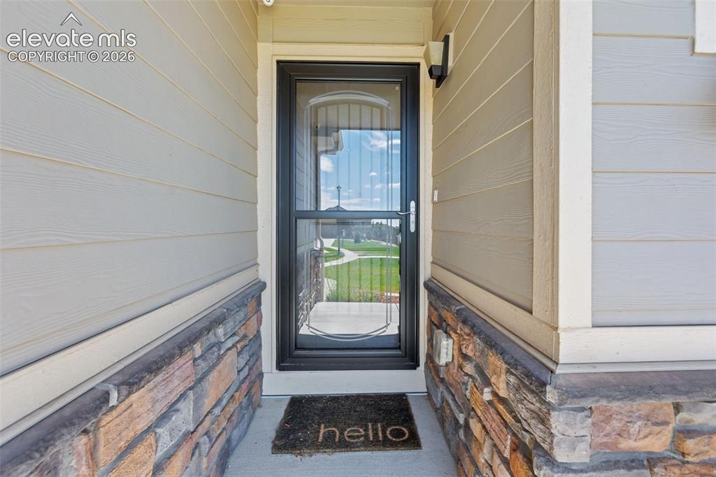 Image 6 of 40: Entryway featuring horizontal siding, stone veneer accents, and a full-ligh
