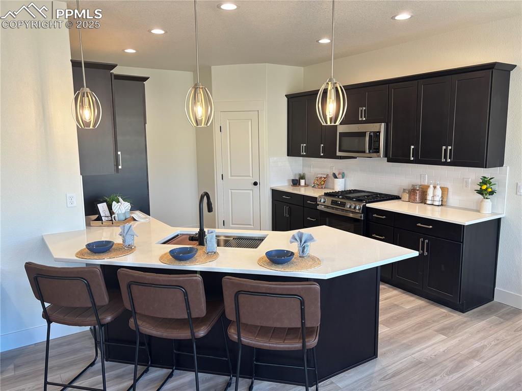 Image 8 of 19: Kitchen featuring dark cabinetry, a breakfast bar, a peninsula, stainless s