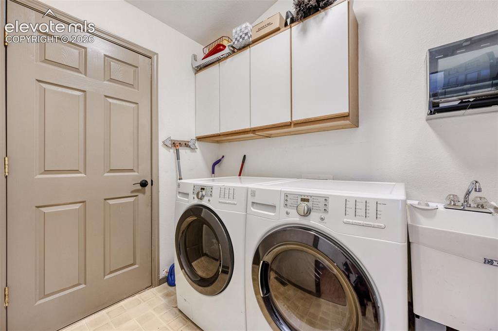 Image 24 of 29: Dedicated laundry area featuring a utility sink, upper cabinetry with wood-