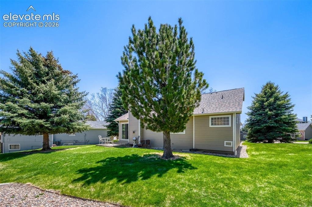 Image 28 of 29: Expansive green lawn with mature evergreen trees, a tan-sided residence, an