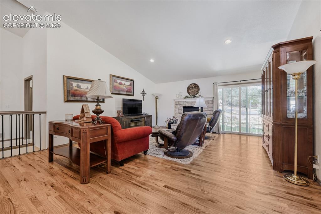 Image 7 of 29: Vaulted ceiling living area featuring wood-finish flooring, a stone-surroun