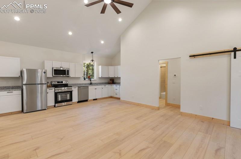 Image 14 of 37: Kitchen featuring a barn door, high vaulted ceiling, white cabinets, applia