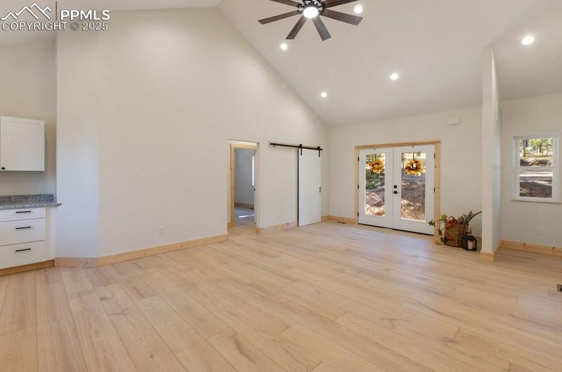 Image 8 of 37: Unfurnished living room with a barn door, high vaulted ceiling, light wood-